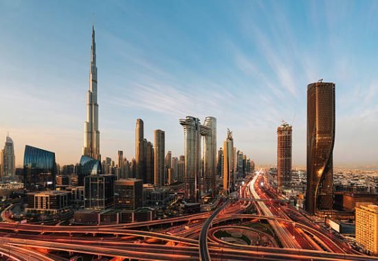Aerial view of Dubai skyline at sunset. Burj Khalifa and road intersection with traffic lights.